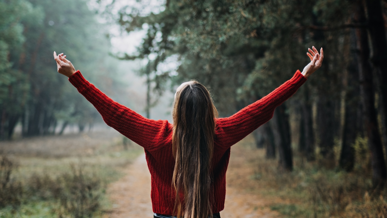 Woman standing in nature with arms raised, symbolizing resilience and mental health recovery