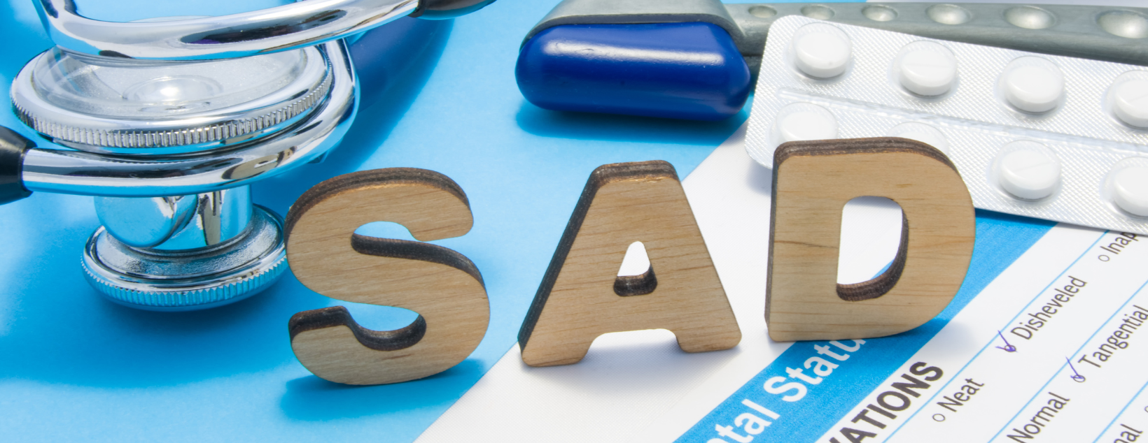 Wooden letters spelling "SAD" alongside a stethoscope, brain model, and medication, symbolizing medical treatment for Seasonal Affective Disorder.