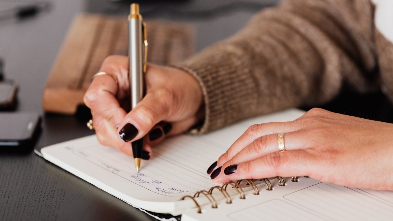 Close-up of a woman’s hands journaling for mental health, capturing the practice of self-reflection, emotional clarity, and personal growth through writing.