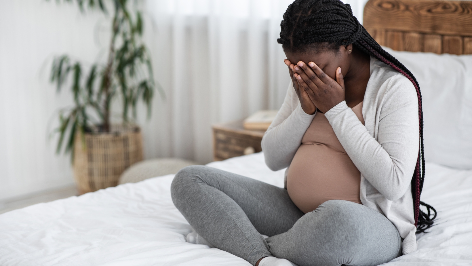 A pregnant parent holding hands to face in despair.