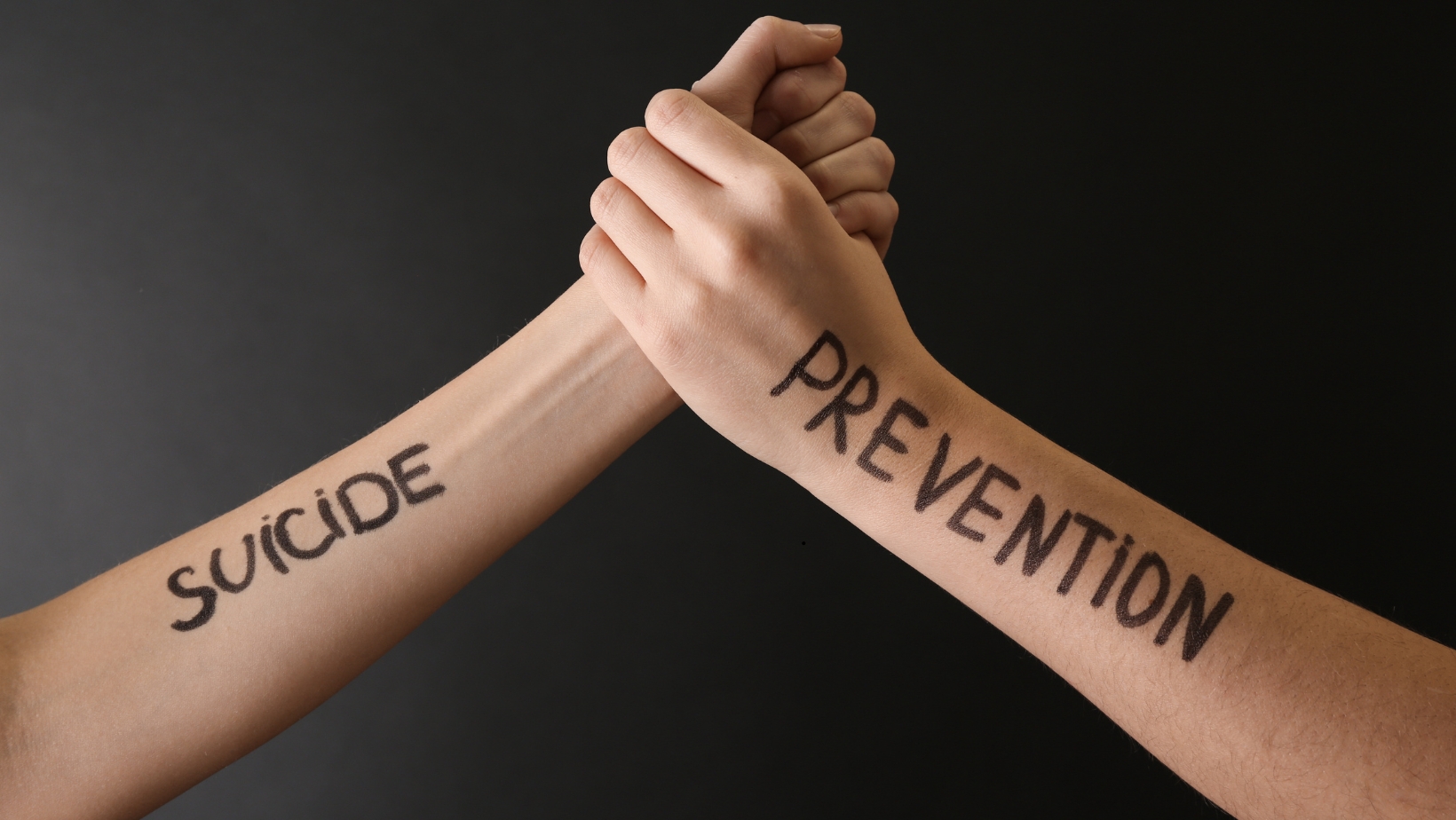 Two clasped hands with the words suicide and prevention written on forearms, symbolizing support and awareness for September Suicide Prevention Month.