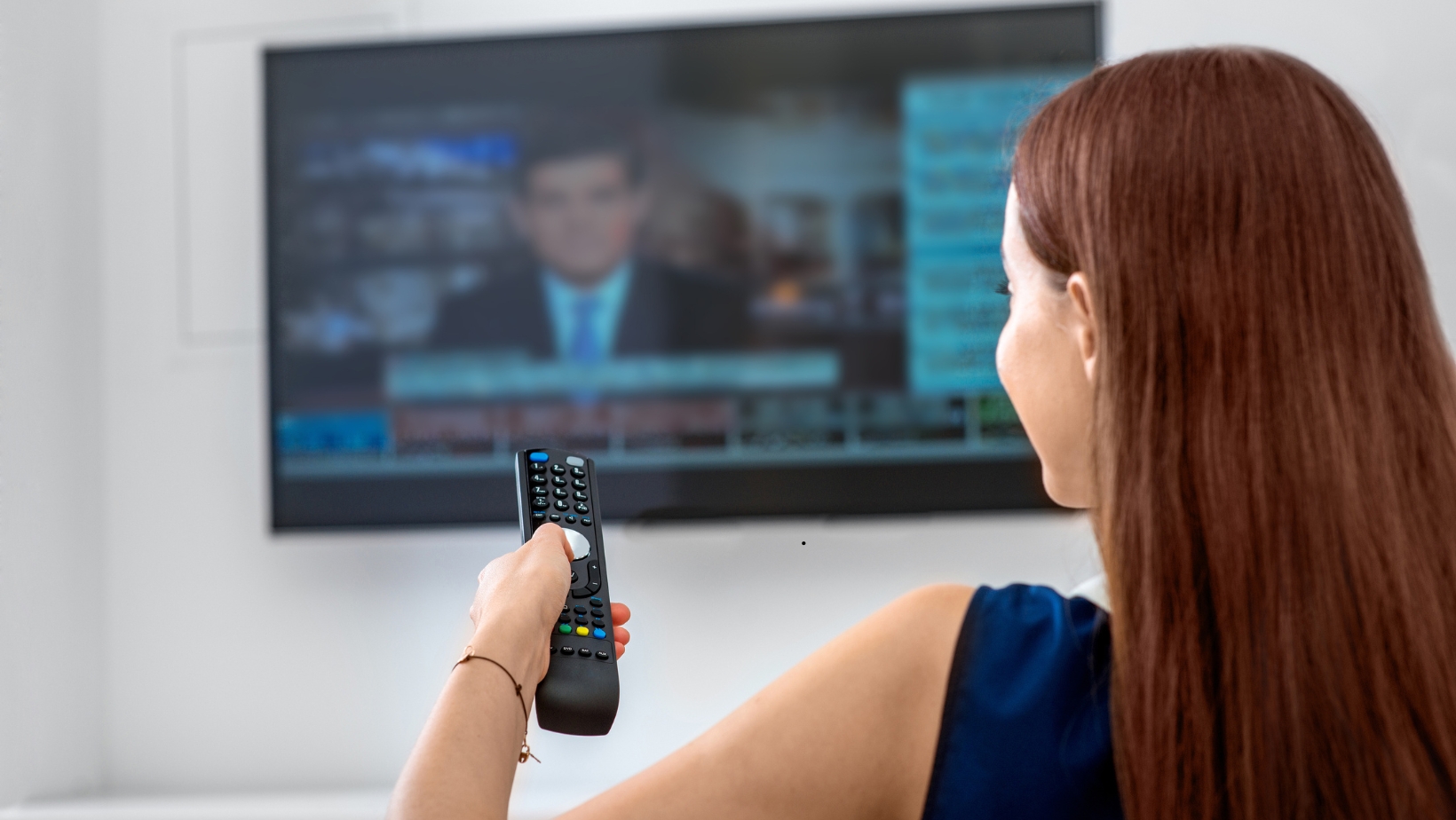 Woman holding a remote control while watching a news broadcast on television at home.