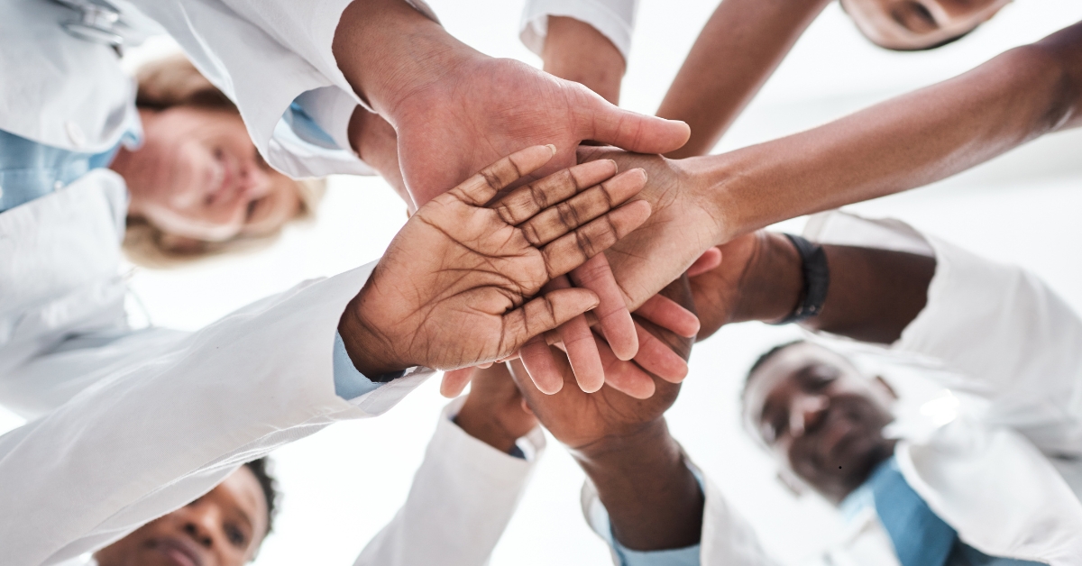 Diverse group of healthcare professionals joining hands in a team huddle, symbolizing collaboration and patient-centered care.