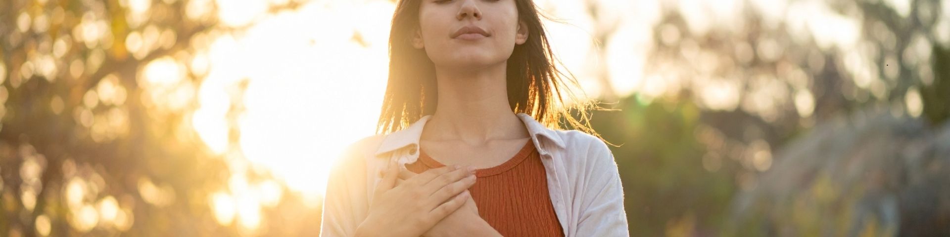 Person standing quietly in sunlight with eyes closed, hands resting gently in their lap, illustrating mindfulness practice as a structured clinical tool for stress, anxiety, and depression.