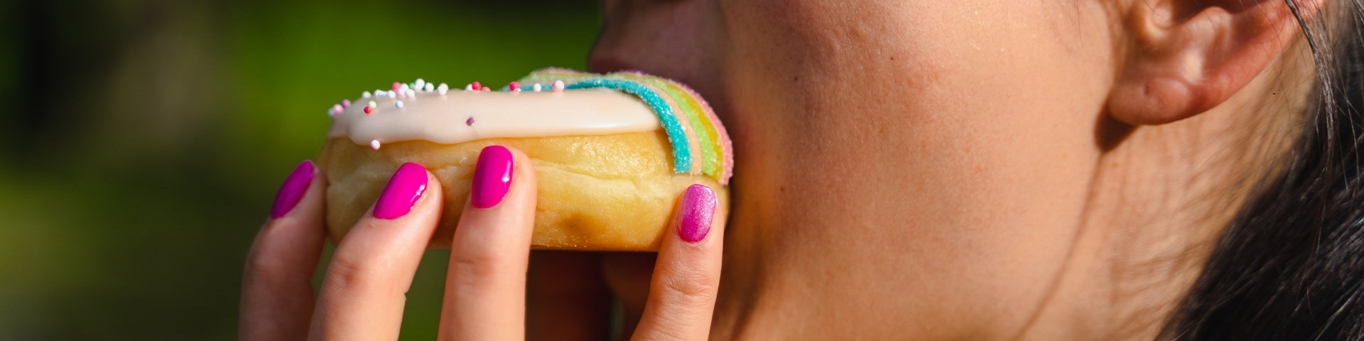 Female with pink nails eating a donut showing the drive of cravings for food, and other substances.